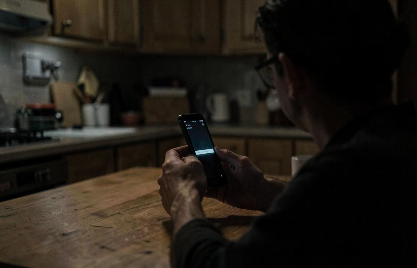 A person at a kitchen table at night holding a phone